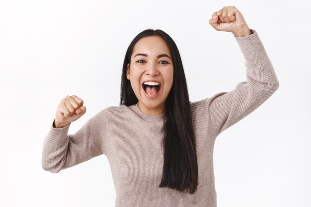 Allegra ragazza asiatica eccitata che fa il tifo per la squadra di calcio, alza le mani in alto, pompa a pugno e sorride, grida dall'adorazione e dal brivido, il fan devoto vuole vincere. Donna che trionfa come competizione per diventare campione