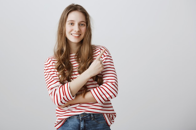 Allegra ragazza carina che punta il dito nell'angolo in alto a destra e sorridente soddisfatto