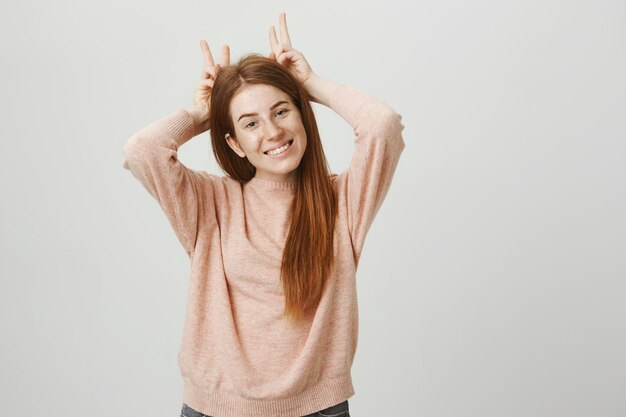 Allegra ragazza carina rossa che mostra le corna in alto sopra la testa e sorridente