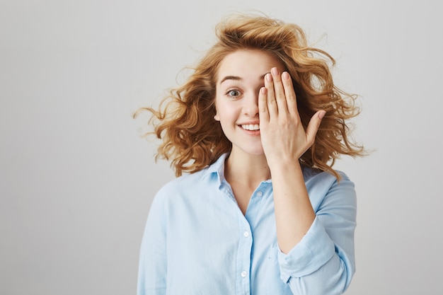 Allegra ragazza dai capelli ricci copre metà del viso e sorridente