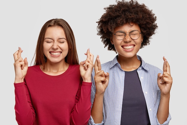 Allegri due compagni di gruppo femminili di razza mista incrociano le dita per buona fortuna