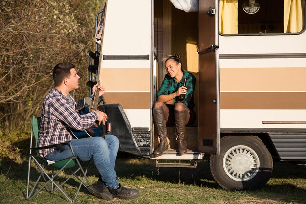 Allegri godendo il loro tempo insieme nella foresta di montagna con il loro camper retrò. Fidanzato che suona una canzone alla chitarra per la sua ragazza.