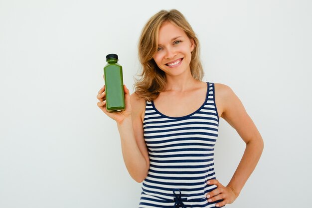 Allegro bella giovane donna che raccomanda buon shampoo e guardando la fotocamera contro sfondo bianco. Ritratto di donna felice tenendo la mano sul fianco e mostrando nuovo prodotto. Concetto di scelta