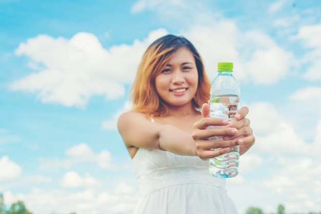 Allegro giovane donna che mostra una bottiglia di acqua con tappo verde