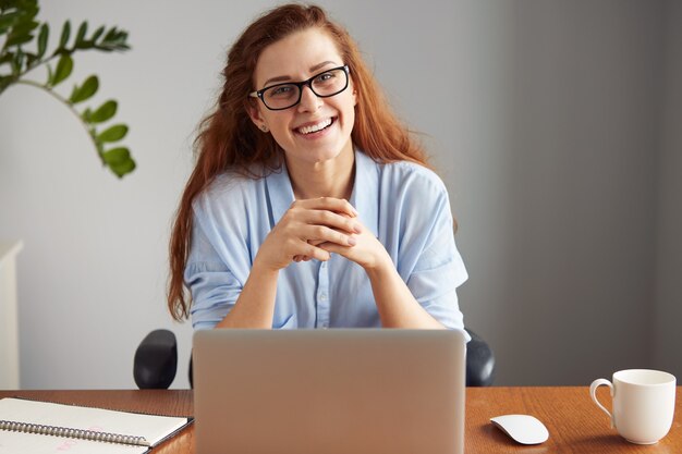 Allegro giovane imprenditrice in camicia casual e bicchieri alla ricerca e sorridente