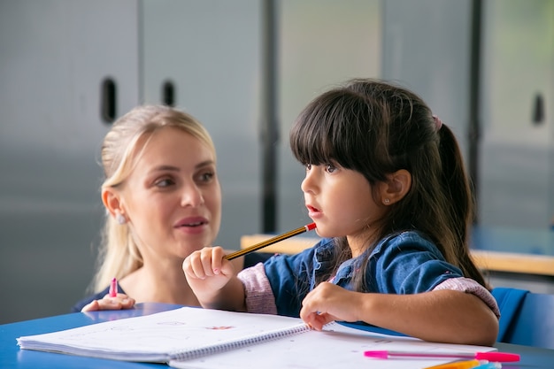 Allegro giovane insegnante di scuola aiutando la piccola scolara a fare il suo compito