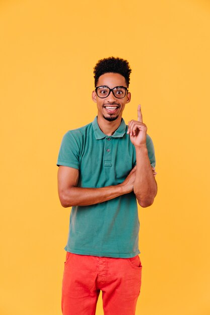 Allegro ragazzo nero in grandi bicchieri che esprimono emozioni positive. Tiro al coperto di elegante uomo africano indossa pantaloni rossi.