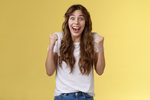 Allegro solidale felice divertimento femminile pompa pugno sollevato trionfante tifo tifo per la squadra preferita vincente sorridente ampiamente si spera guardare fotocamera celebrando vittoria sfondo giallo