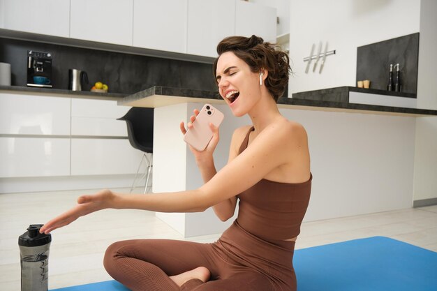 allenamento da casa felice giovane bruna ragazza di fitness si siede sul pavimento della cucina tappetino da yoga con bottiglia d'acqua