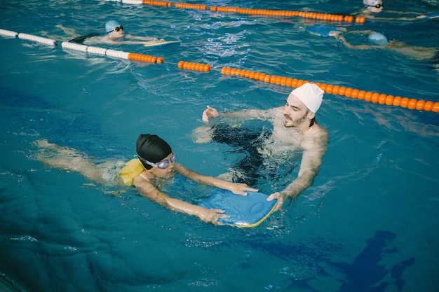 Allenatore che insegna al bambino nella piscina coperta come nuotare e tuffarsi. Lezione di nuoto, sviluppo dei bambini.