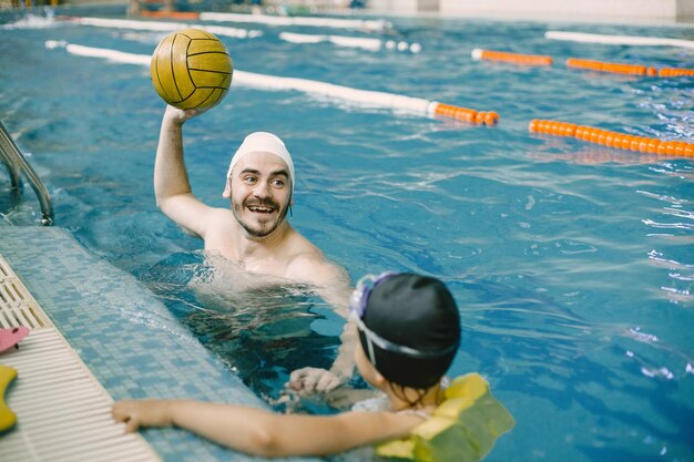 Allenatore che insegna al bambino nella piscina coperta come nuotare e tuffarsi. Lezione di nuoto, sviluppo dei bambini.