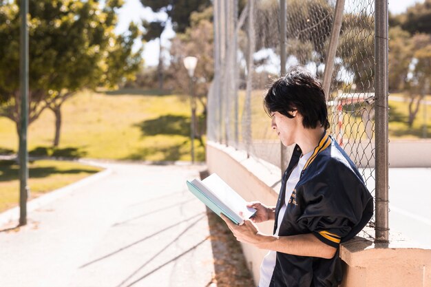 Allievo etnico lettura libro al vicolo nel parco