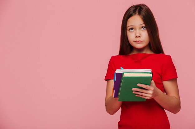 Allievo pensieroso della ragazza che esamina lo spazio della copia e che tiene i libri