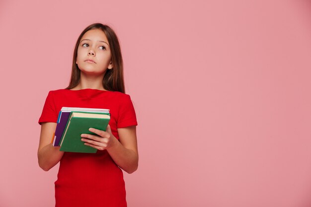 Allievo pensieroso della ragazza che esamina lo spazio della copia e che tiene i libri