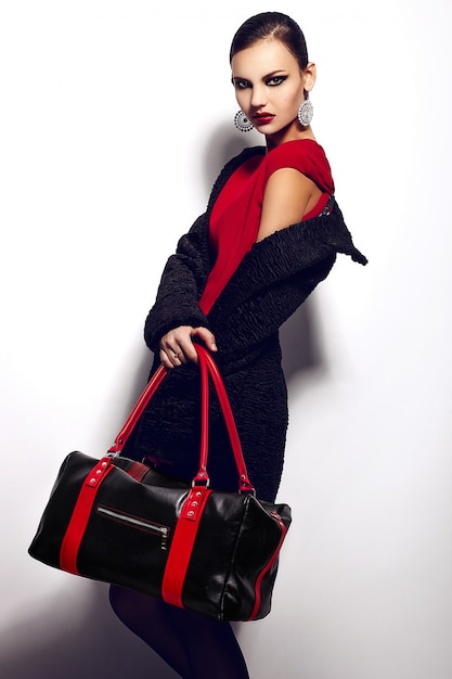 Alta moda look.glamor closeup ritratto di bella sexy elegante bruna caucasica giovane donna modello in abito rosso con borsa nera trucco luminoso, con labbra rosse, con una pelle pulita perfetta in studio