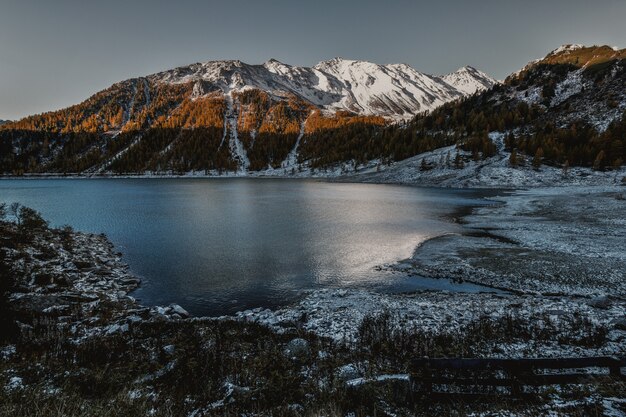 Alta montagna marrone e bianca accanto al corpo di acqua