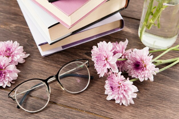 Alto angolo dei fiori e dei vetri dei libri sulla tavola di legno