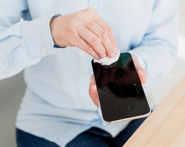 Alto angolo della donna più anziana che disinfetta il suo smartphone