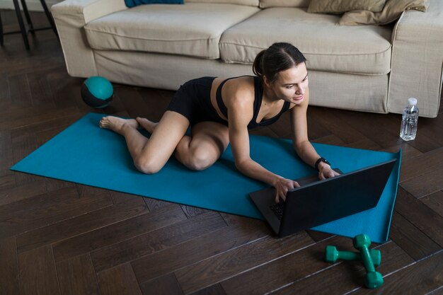 Alto angolo della femmina con il computer portatile sulla stuoia di yoga