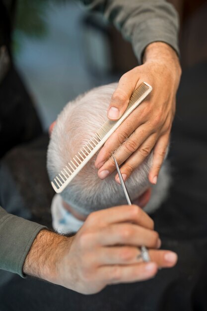 Alto angolo di barbiere che dà al cliente maschio anziano un taglio di capelli