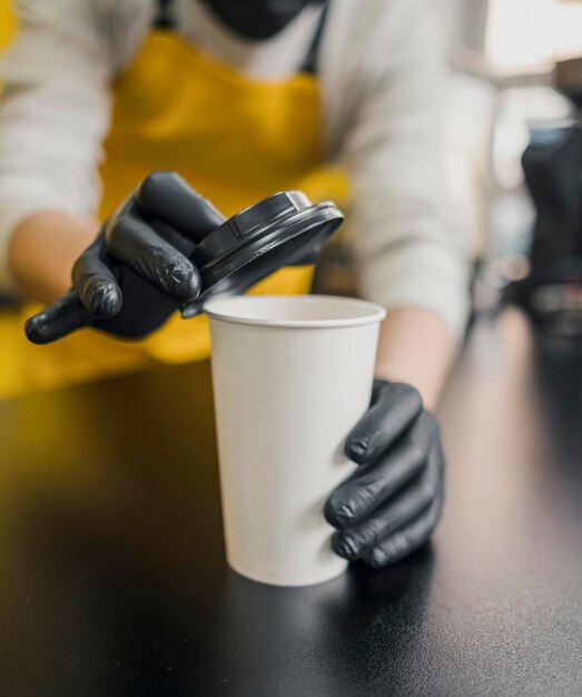 Alto angolo di barista con guanti in lattice che mettono il coperchio sulla tazza di caffè