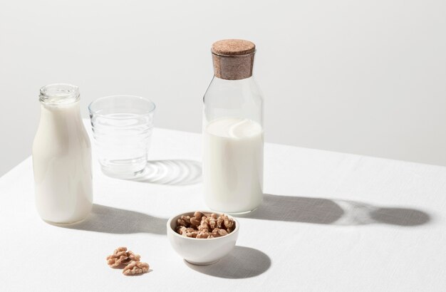 Alto angolo di bottiglia per il latte con bicchiere vuoto e ciotola di noci