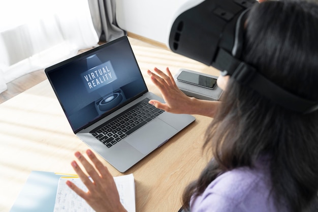 Alto angolo di donna che utilizza le cuffie da realtà virtuale a casa con il laptop