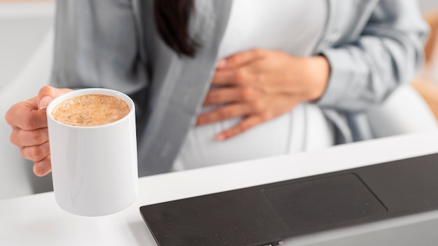 Alto angolo di donna incinta con laptop e tazza di caffè che lavorano da casa