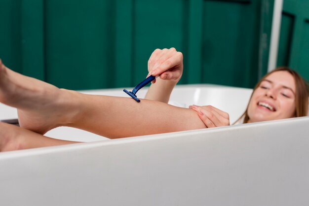 Alto angolo di donna nella vasca da bagno che si rade le gambe
