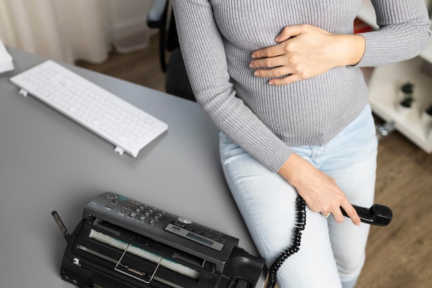 Alto angolo di imprenditrice incinta con il telefono in ufficio