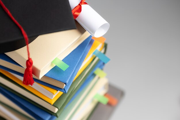Alto angolo di libri impilati, un cappello di laurea e un diploma per la giornata dell'istruzione