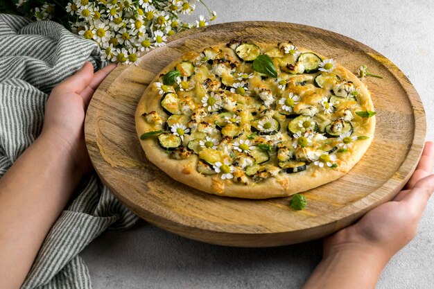 Alto angolo di persona che tiene una deliziosa pizza cotta con bouquet di fiori di camomilla