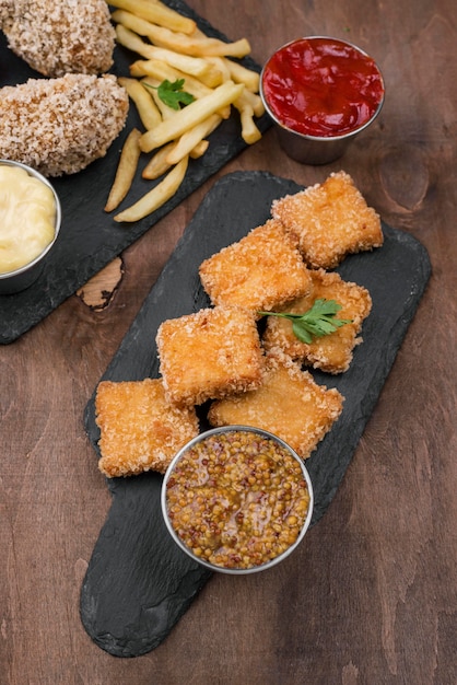 Alto angolo di pollo fritto su ardesia con patatine fritte e salsa