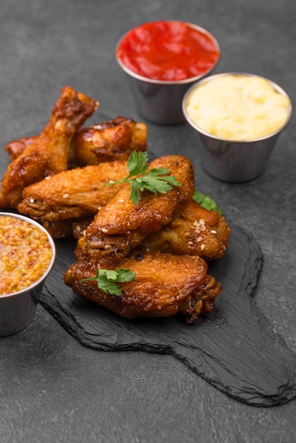 Alto angolo di pollo fritto su ardesia con varietà di salse