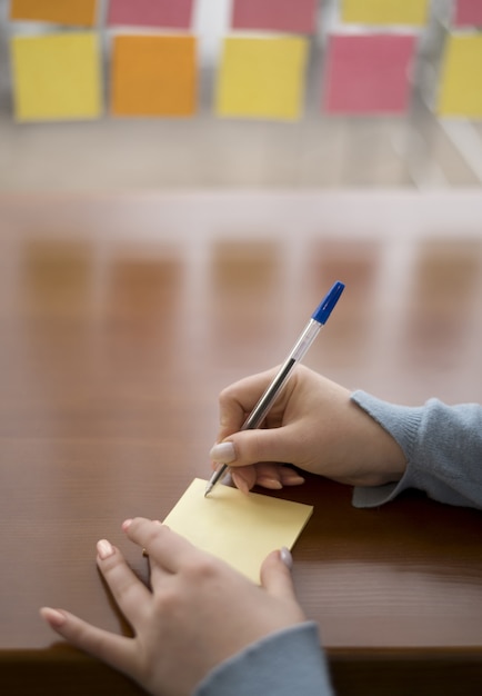 Alto angolo di scrittura della donna sulle note appiccicose mentre all'ufficio