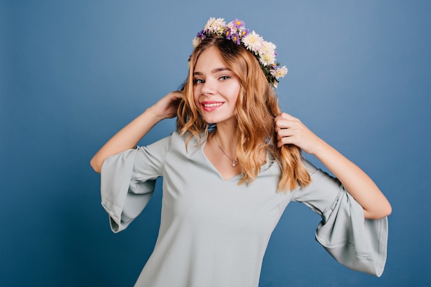 Amabile donna bianca in ghirlanda di fiori che balla sulla parete blu