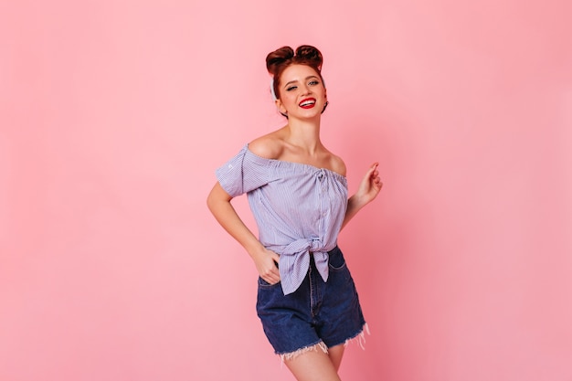 Amabile ragazza dello zenzero in shorts in denim che ride alla macchina fotografica. Studio shot di adorabile donna pinup isolata su uno spazio rosa.