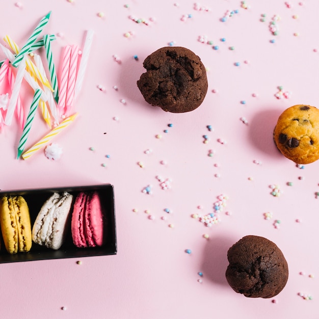 Amaretti multicolori; candele; muffin dolci; pastello spruzza su sfondo rosa