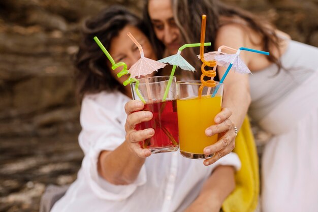 Amiche anziane che applaudono con cocktail in spiaggia