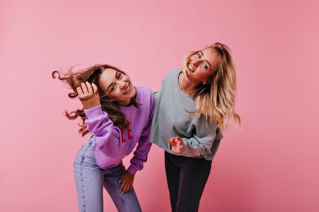 Amiche di buon umore in jeans che esprimono felicità. Magnifiche sorelle che ridono sulla porpora.