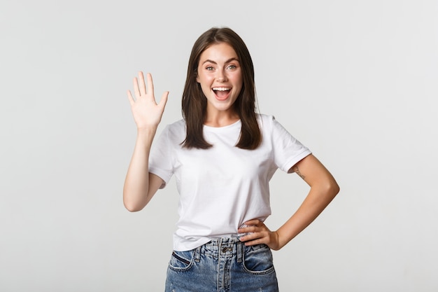 Amichevole ragazza sorridente agitando la mano per dire ciao, salutando qualcuno.