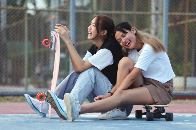 Amici adolescenti felici di due ragazze asiatiche con lo skateboard al sole che giocano insieme il giorno d'estate e lo stile di vita dello skateboard