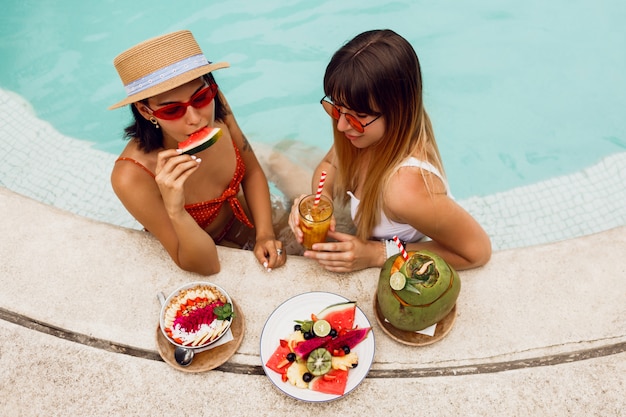 Amici beati svegli che godono del cibo vegano saporito in stagno durante la vacanza tropicale in Bali. Piatto di frutti esotici. Atmosfera da festa.