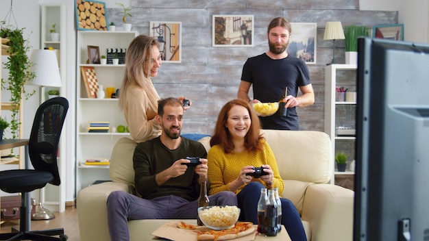 Amici caucasici allegri che giocano ai videogiochi su una grande tv in soggiorno.