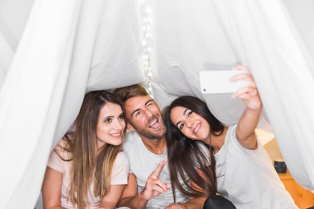 Amici che assumono selfie sul cellulare seduto sotto la tenda