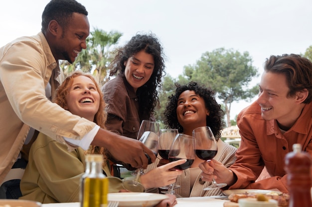 Amici che brindano con bicchieri di vino e mangiano barbecue durante la festa all'aperto