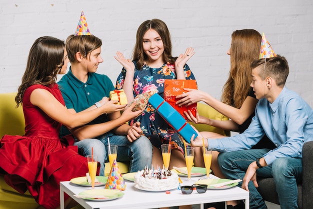 Amici che danno scatole regalo avvolte alla ragazza eccitata del compleanno