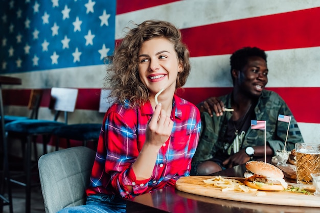 Amici che riposano insieme al bar, donne e uomini al bar, parlando, ridendo mangiano fast food.