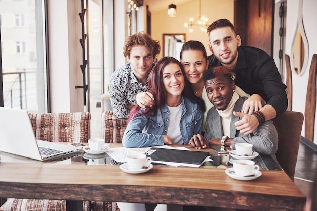 Amici che si divertono al ristorante. Tre ragazzi e due ragazze che fanno selfie e ridono.