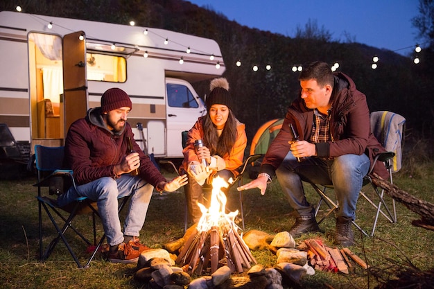 Amici che si scaldano le mani intorno al fuoco da campo dopo un'escursione in montagna. Camper retrò.